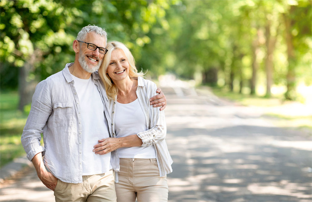 Beautiful mature spouses hugging outdoors while walking in summer park
