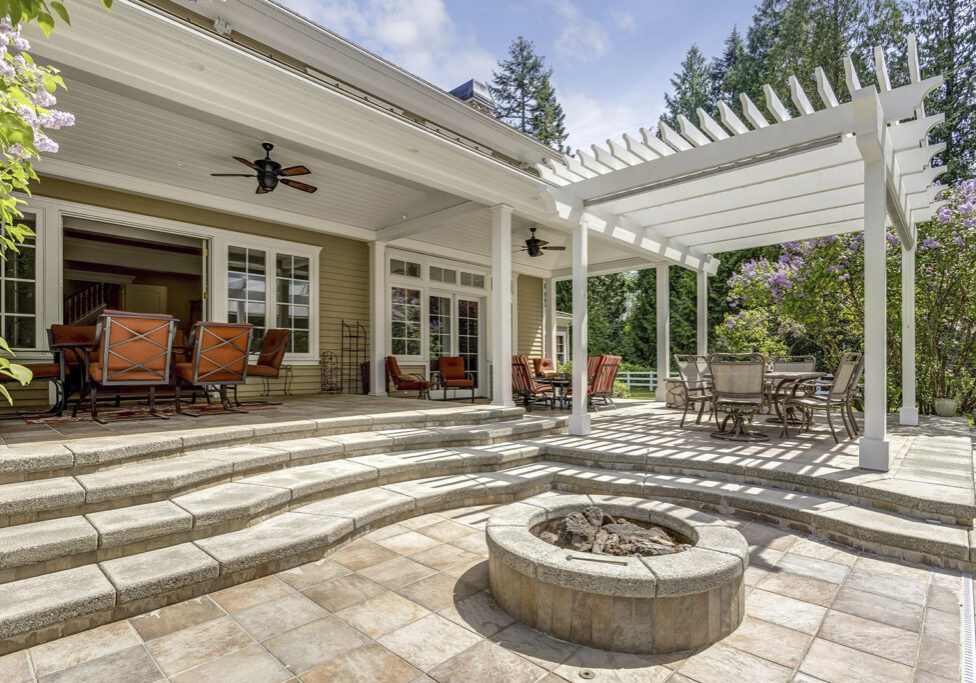 Lovely outdoor deck patio space with white pergola, fire pit in the backyard of a luxury house.